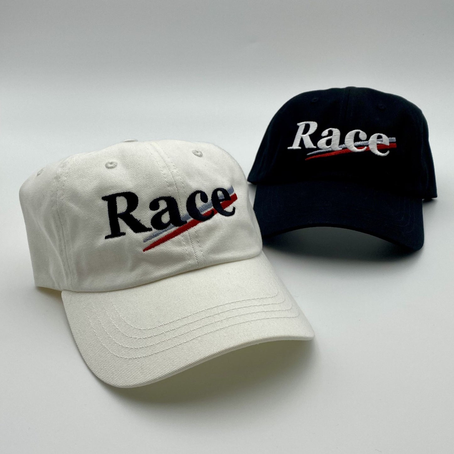 Two hats, one white and one black, with 'Race' embroidered on them against a light gray background.