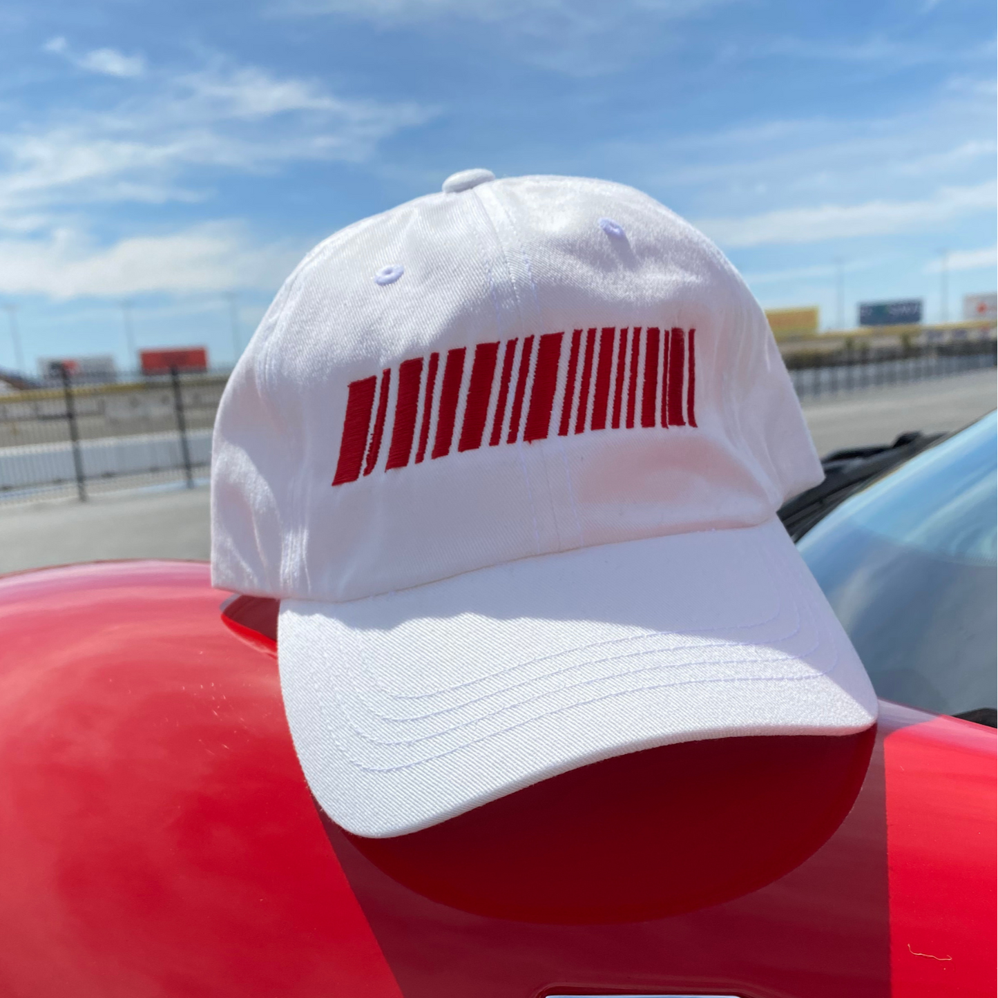 White cap with red barcode design on a red car against a blue sky.