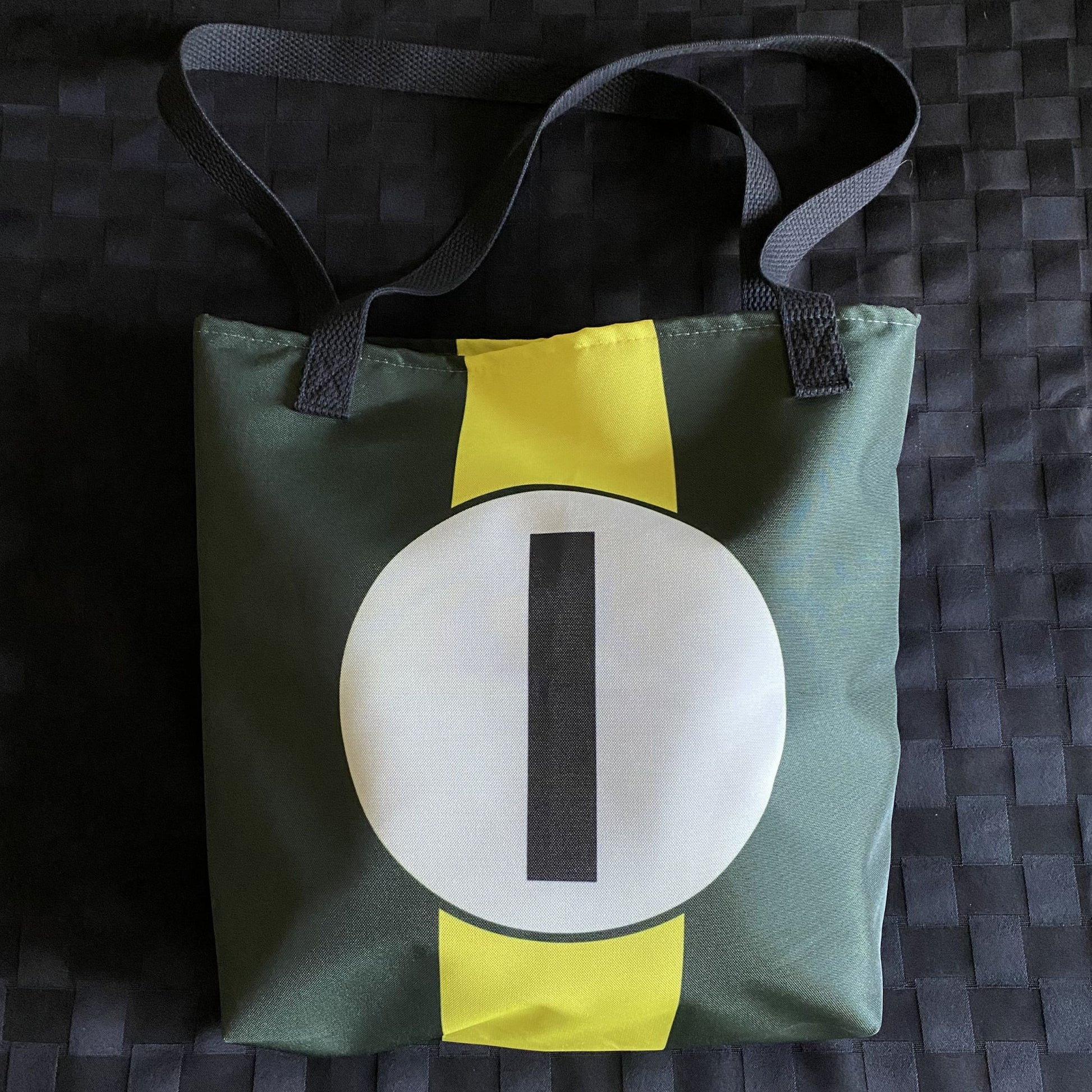 Green tote bag with a yellow racing stripe and number "1" in a white circle on a textured surface