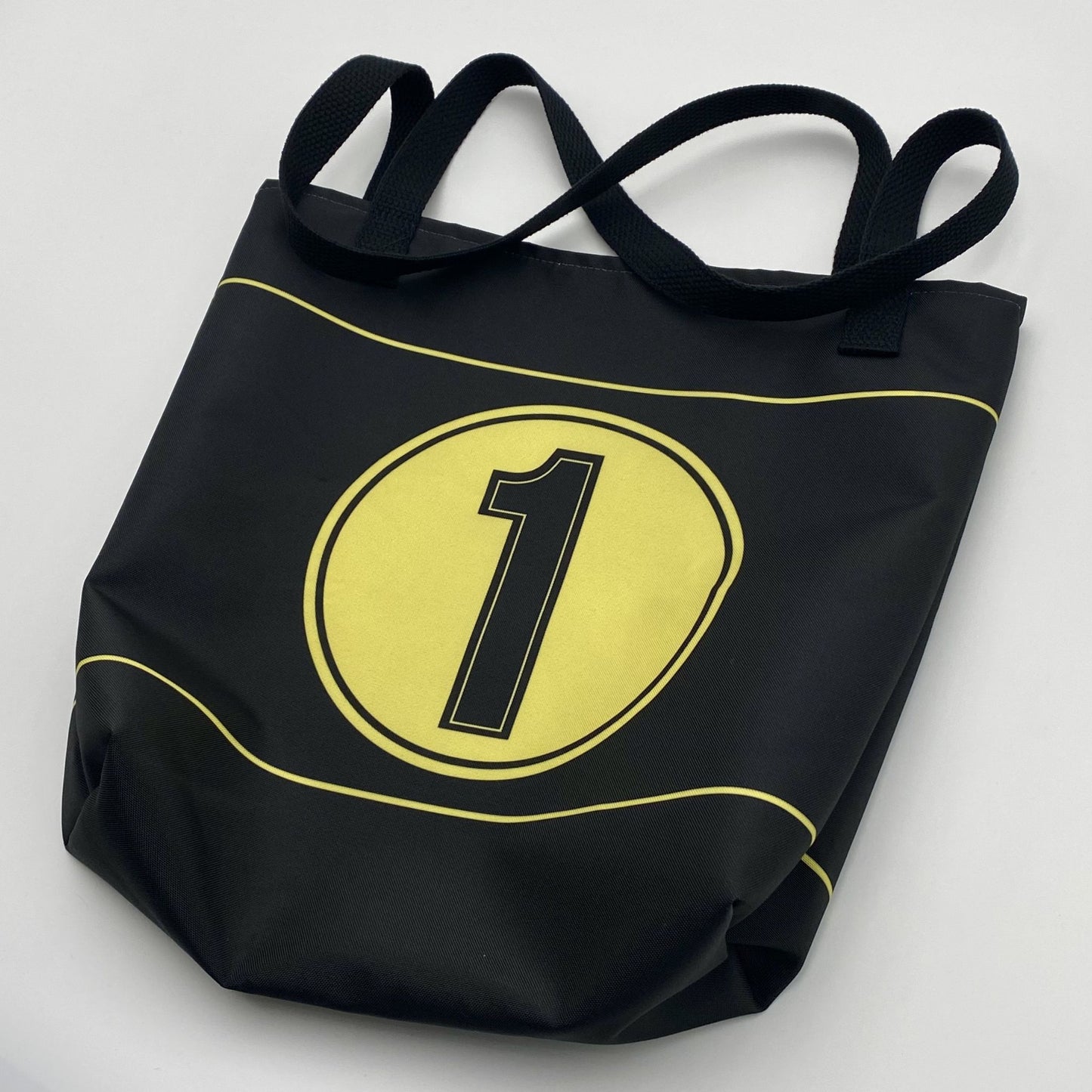Black tote bag with gold stripes, circle and black number '1' on a light gray background