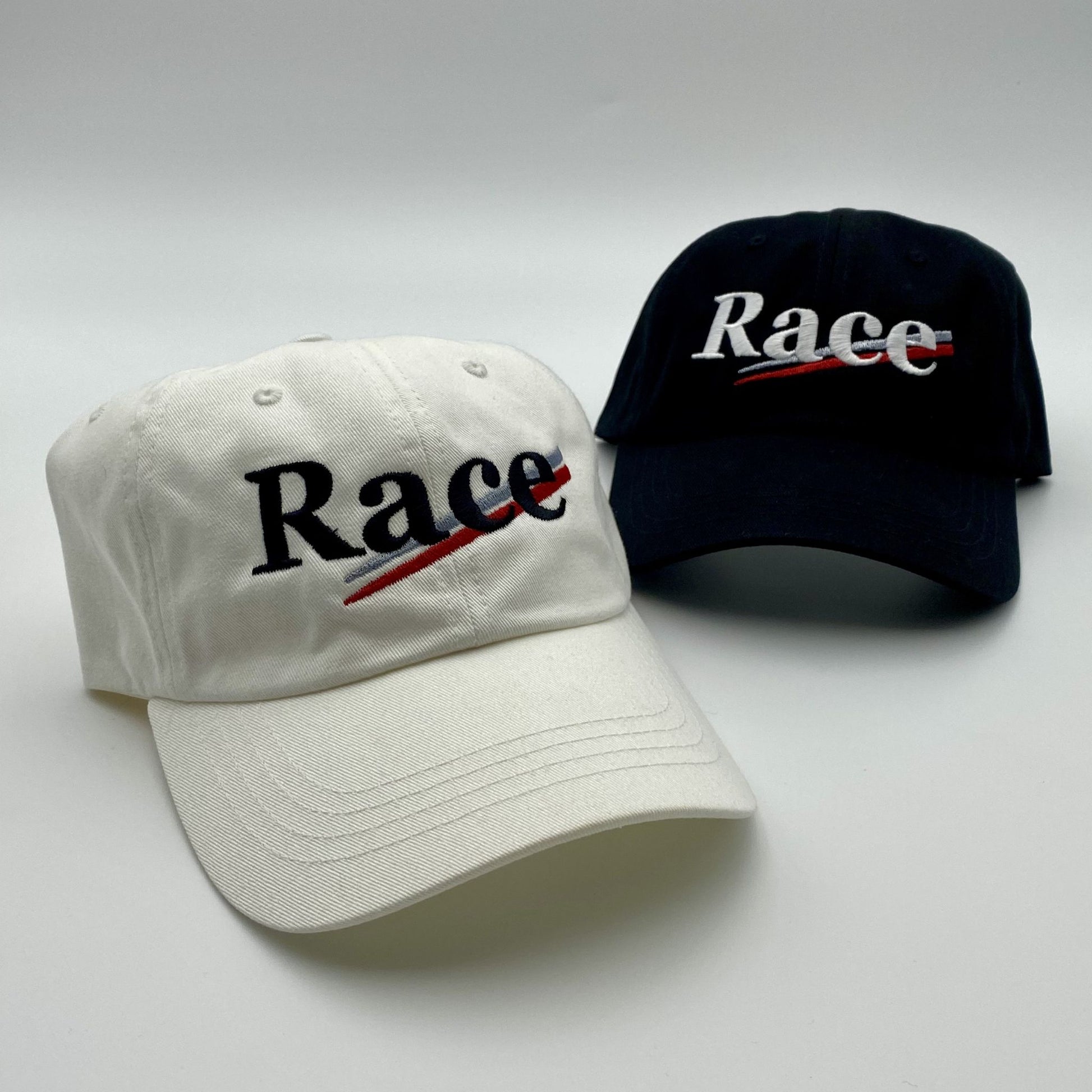 Two hats, one white and one black, with 'Race' embroidered on them against a light gray background.