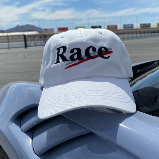 White cap with 'Race' text in black with silver and red stripes on a car at a race track